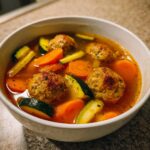 Close-up of a white bowl filled with flavorful albondigas soup, featuring meatballs, sliced carrots, and zucchini chunks.