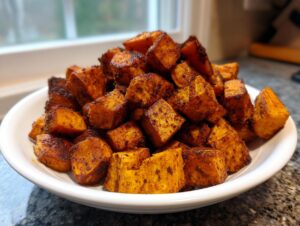 A close-up of a white bowl piled high with perfectly seasoned and browned roasted sweet potatoes.