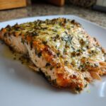 Close-up of a flaky, golden-brown air fryer salmon fillet topped with melted cheese and fresh herbs.