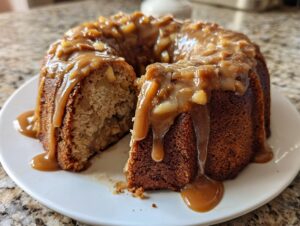 A slice cut from a moist apple bundt cake topped with thick caramel sauce and chopped apples.