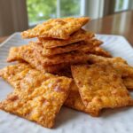 A close-up pile of golden brown, flaky homemade cheese crackers sprinkled with coarse salt.