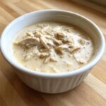 A close-up of rich, creamy cream of chicken soup loaded with shredded chicken in a white bowl.