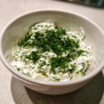 A close-up of creamy, white dill dip topped generously with fresh chopped dill.