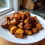 A pile of perfectly seasoned, golden-brown roasted sweet potatoes cubes served on a white plate.