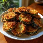 A pile of crispy, golden brown baked parmesan zucchini slices served on a white plate.