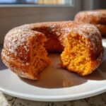 A close-up showing the fluffy interior of a baked pumpkin donut, broken in half and coated in sugar.