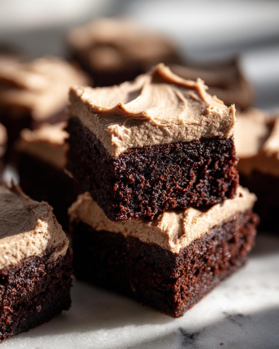Close-up of stacked, fudgy banana bread brownies topped with light brown frosting.