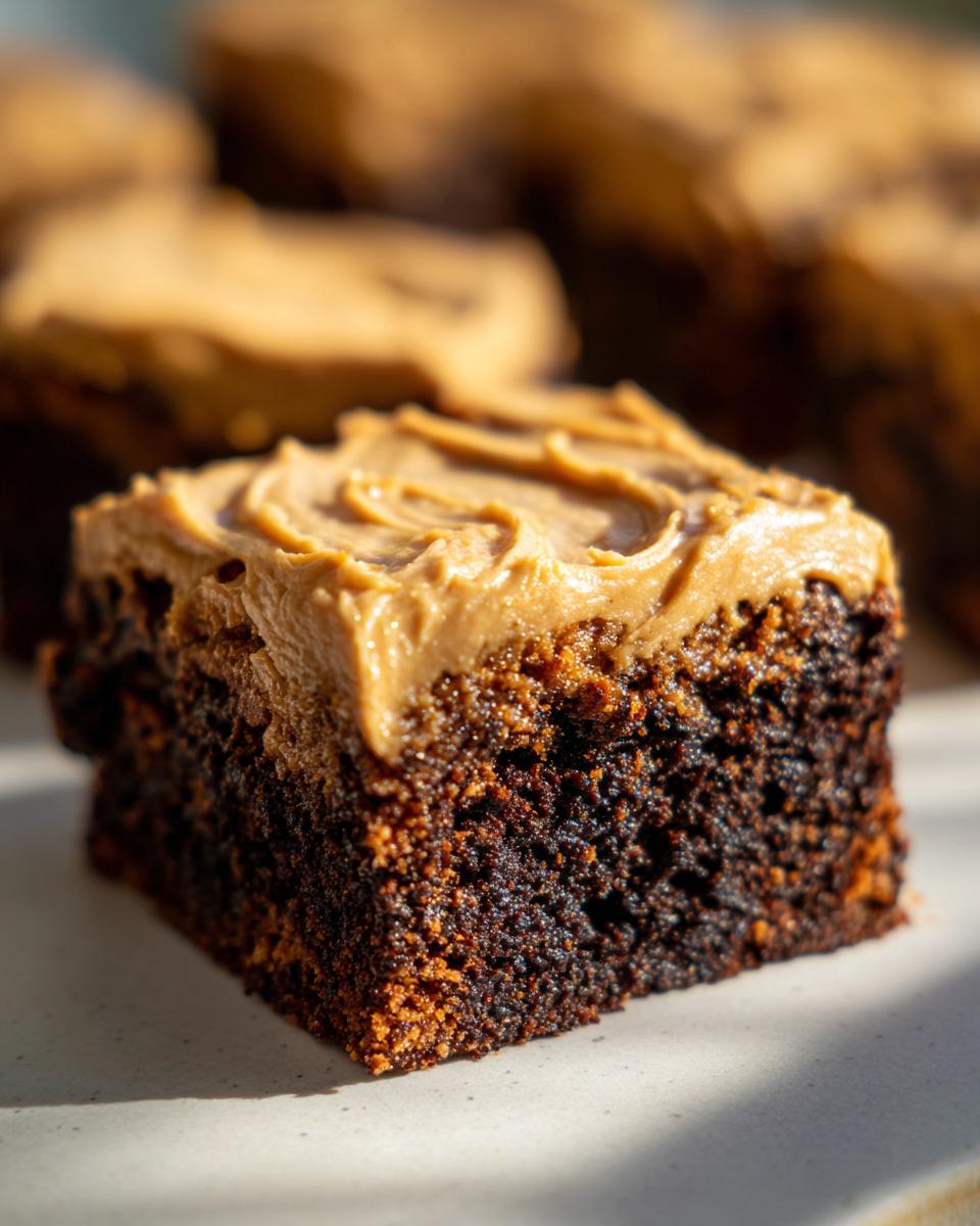 A close-up, sunlit shot of a rich, dark square of banana bread brownies topped with creamy peanut butter frosting swirls.