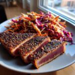 Three thick slices of blackened tuna steak, perfectly seared with a pink center, served next to a colorful slaw.