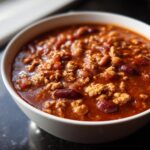 Close-up of a white bowl filled with rich, saucy high protein chili featuring ground meat and kidney beans.