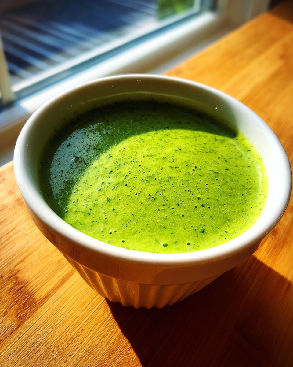 A vibrant, bright green cilantro lime sauce with a slightly frothy texture in a white ceramic bowl.
