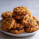 A tempting stack of freshly baked brown butter oatmeal raisin cookies piled high on a white plate.