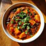A vibrant bowl of butternut squash chili featuring large chunks of orange squash and black beans, topped with fresh cilantro.