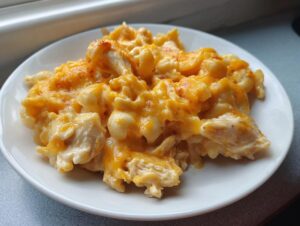 Close-up of a white plate piled high with creamy, cheesy chicken pasta topped with melted orange cheddar.