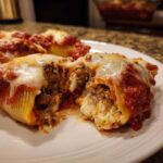 Close-up of a cheesy, meat-filled stuffed shells pasta, cut open to show the rich filling and melted mozzarella topping.