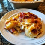 A generous serving of cheesy pierogi casserole topped with crispy bacon on a white plate.