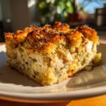 A close-up of a square serving of creamy chicken and wild rice casserole with a golden, herbed breadcrumb topping.