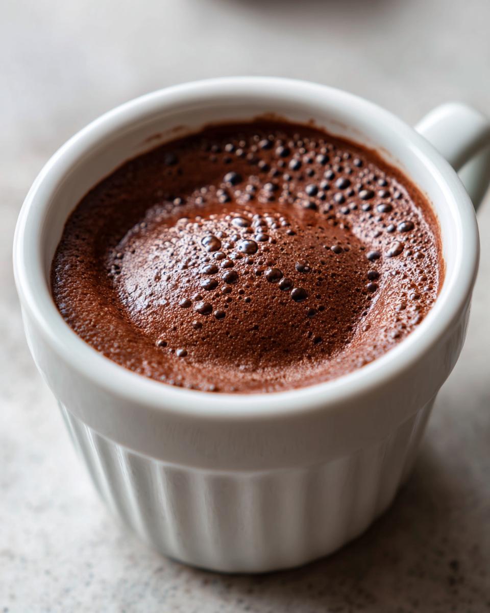 Close-up of airy, dark brown chocolate mousse topped with small bubbles in a white fluted ramekin.