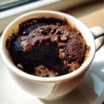 Close-up of a rich, dark chocolate mug cake topped with chocolate chips, ready to eat.