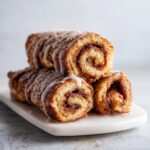Close-up of stacked cinnamon roll french toast pieces drizzled with white icing.