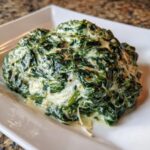 A close-up serving of rich, homemade creamed spinach recipe on a white rectangular plate.