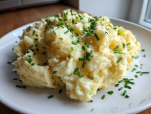 A generous serving of creamy garlic mashed potatoes topped with melted butter and fresh chopped chives on a white plate.