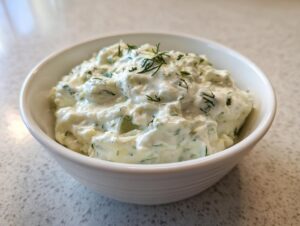 Close-up of a white bowl filled with creamy, chunky pickle dip garnished with fresh dill.