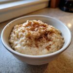 A close-up of a bowl of creamy rice pudding generously sprinkled with ground cinnamon.