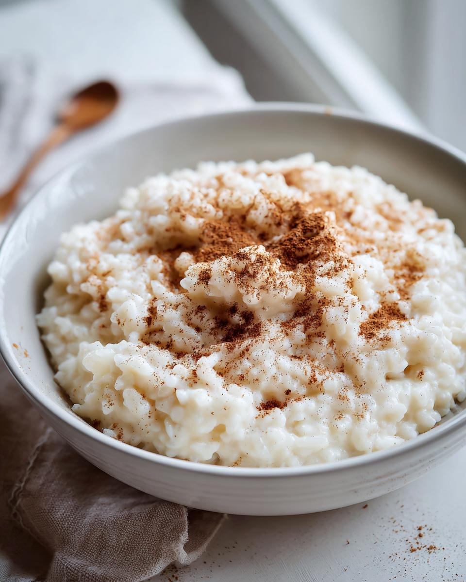 Close-up of creamy rice pudding in a white bowl, generously topped with ground cinnamon.