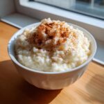 A close-up of creamy rice pudding recipe served in a white bowl, generously topped with ground cinnamon.
