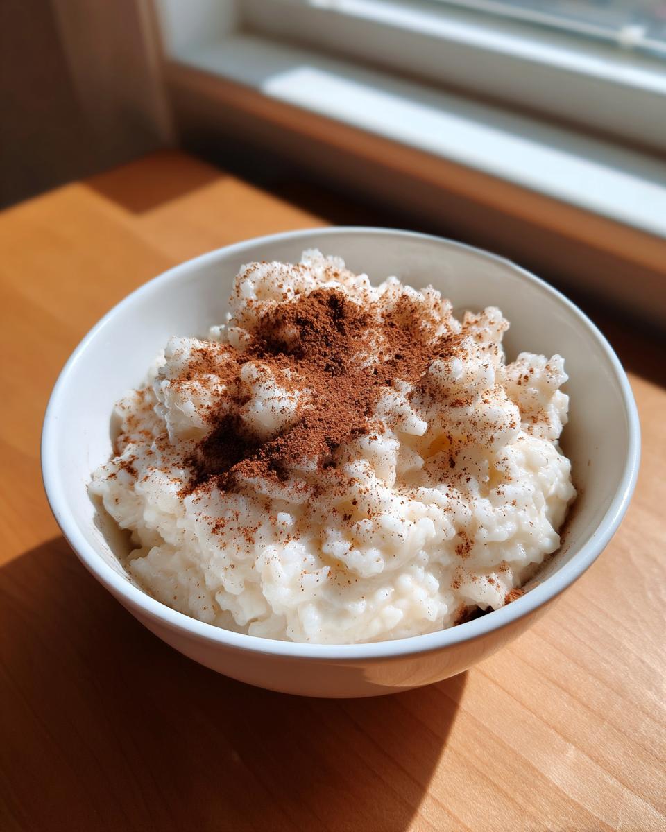 A white bowl filled with creamy rice pudding recipe, generously dusted with ground cinnamon.