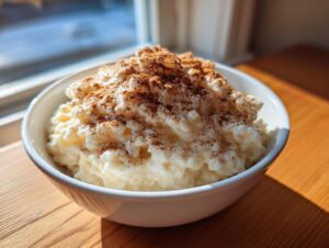 A close-up of a white bowl filled with creamy rice pudding recipe, generously sprinkled with cinnamon.