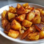 Close-up of perfectly crispy, golden-brown seasoned breakfast potatoes mixed with sautéed onions in a white bowl.