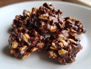 A close-up of several glossy, chocolate-covered clusters made with peanuts, resembling crockpot peanut clusters.