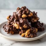A tempting stack of rich, chocolate-covered crockpot peanut clusters piled high on a small white plate.