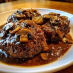 Close-up of three juicy salisbury steak patties smothered in dark mushroom gravy.