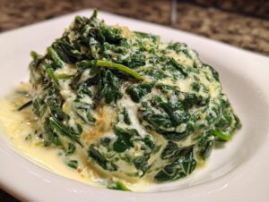 A close-up of a generous serving of rich creamed spinach recipe piled high on a white plate.