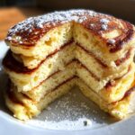 Cross-section view showing the incredibly fluffy texture inside a stack of golden brown pancakes dusted with powdered sugar.