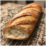 Close-up of a golden-crusted french bread loaf with a soft interior, cooling on a wire rack.