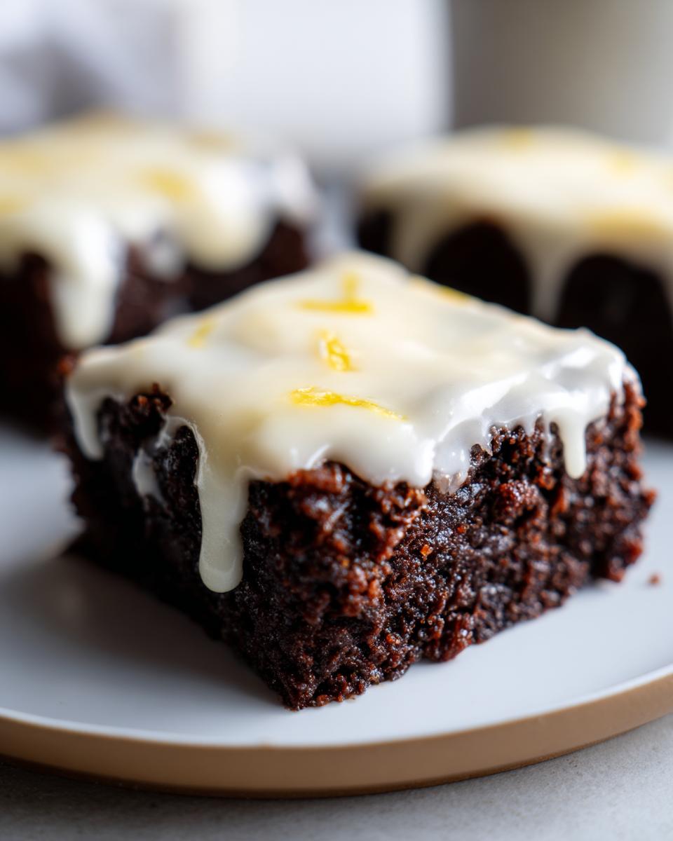 Close-up of a fudgy Lemon Brownies square topped with dripping white glaze and lemon zest.