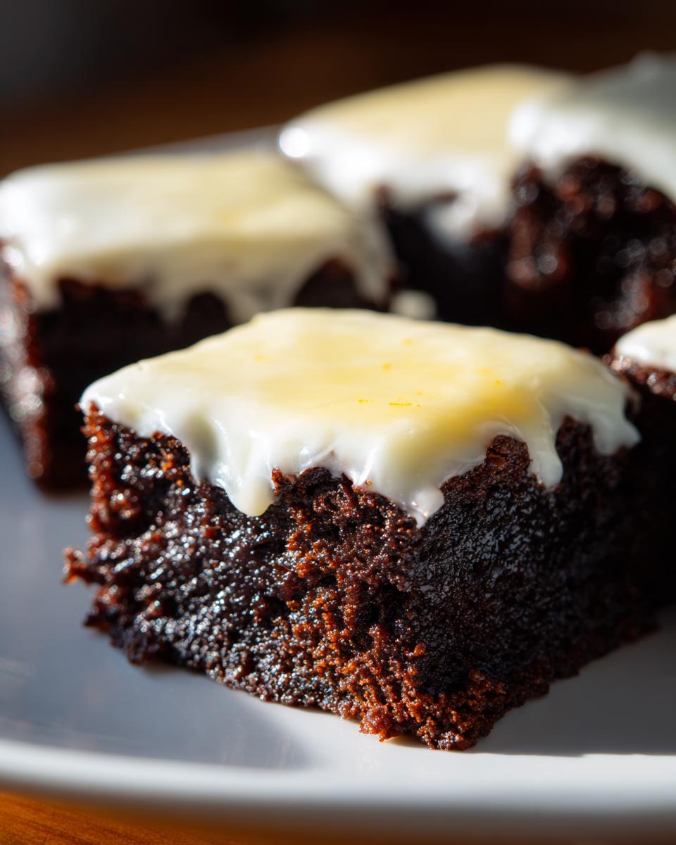 Close-up of a fudgy, dark chocolate square topped with a thick white glaze, representing a Lemon Brownies recipe.