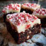 Close-up of a fudgy peppermint brownie square topped with white frosting and crushed candy canes.