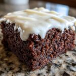 Close-up of a rich, dark brown slice of gingerbread brownies topped with thick white frosting.