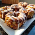 Close-up of several golden brown baked apple fritters drizzled generously with white vanilla glaze.