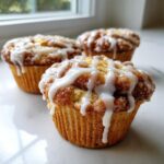 Three freshly baked cinnamon roll muffins topped with a thick, white glaze dripping down the sides.
