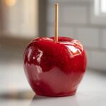 A single, perfectly glossy red candy apple with a wooden stick inserted, ready to eat.