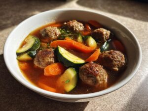 A close-up bowl of homemade albondigas soup featuring meatballs, sliced zucchini, and carrots in a rich broth.