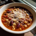 A close-up of a steaming bowl of pasta e fagioli topped generously with grated Parmesan cheese.