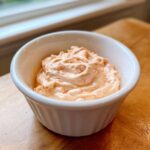 A close-up of creamy, orange-tinted big mac sauce swirled in a small white ramekin.