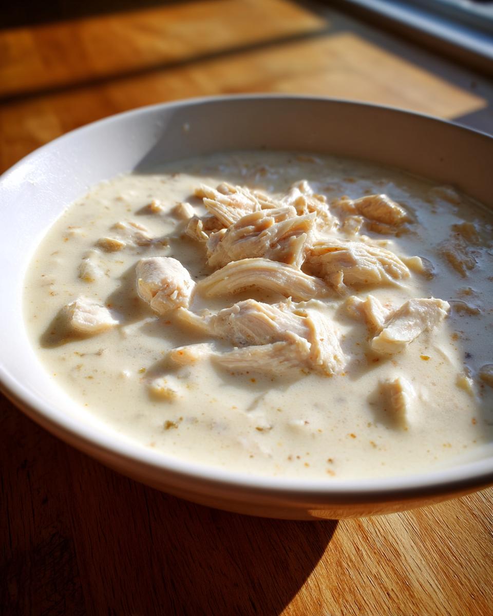 Close-up of a white bowl filled with rich homemade cream of chicken soup topped generously with shredded chicken pieces.